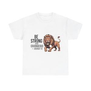 May include: White t-shirt with a brown lion illustration and the text "BE STRONG AND COURAGEOUS - JOSHUA 1:9". The lion has a detailed mane and open mouth. The text is in black, and the overall design is bold.