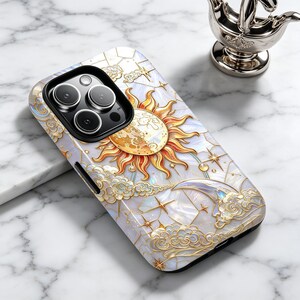 May include: A decorative phone case with a celestial design. It features a sun, moon, stars, and clouds in gold and white. The case has a pearlescent finish and a black camera module.