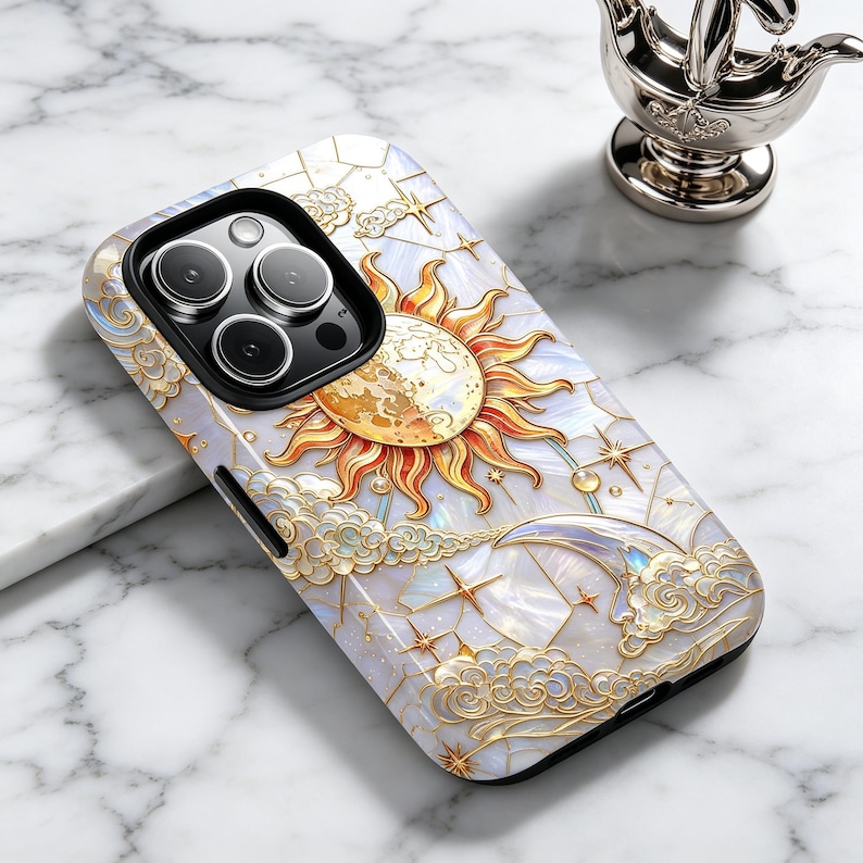 May include: A decorative phone case with a celestial design. It features a sun, moon, stars, and clouds in gold and white. The case has a pearlescent finish and a black camera module.