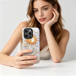 May include: A phone case with a celestial design, featuring a sun, moon, and stars. The case has a white and blue marble effect background with gold detailing. The sun is orange and yellow, and the moon is crescent-shaped with blue and gold.