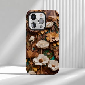 Könnte beinhalten: Eine Smartphone-Hülle mit einem detaillierten Holzmaserungshintergrund, verziert mit einer Vielzahl von dreidimensionalen weißen, cremefarbenen und goldbraunen Blumen, einschließlich großer Blüten und kleiner Knospen, mit Kameraaussparung.