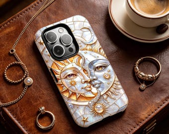 May include: A decorative phone case featuring a sun and moon design with pearl and gold accents. The case is on a brown leather surface, with a gold chain, ring, and a cup of coffee nearby.