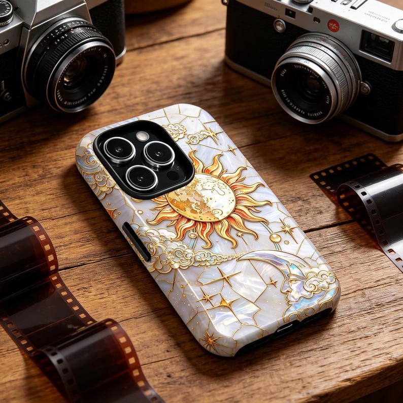 May include: A phone case with a celestial design featuring a sun, moon, stars, and clouds in gold and white. The case is on a wooden surface with film strips and cameras in the background.