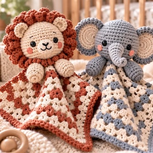 Puede incluir: Dos mantitas de apego tejidas a ganchillo con cabezas de animales de peluche. Uno es un león color crema y óxido con melena texturizada, y el otro es un elefante color crema y azul pizarra con orejas grandes. Ambos tienen caras bordadas y cuerpos.