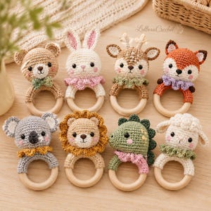 Può includere: Una collezione di otto sonagli all'uncinetto a forma di animale, ognuno con una testa di peluche attaccata a un anello di legno liscio e rotondo. Gli animali includono un orso, coniglio, cervo, volpe, koala, leone, dinosauro e pecora con colletti colorati.