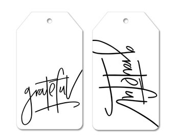 May include: Two white gift tags with black script. One tag reads "grateful" and the other reads "thankful". The tags have a hole at the top for string. The Peach St Design Co. logo is at the bottom.