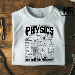 Pode incluir: Camisola branca de gola redonda com a palavra "PHYSICS" em preto, com uma fonte desgastada. A camisa apresenta fórmulas e diagramas científicos, incluindo E=mc², e a frase "WHY STUFF DOES OTHER STUFF".