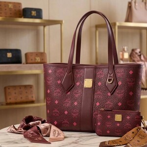 May include: Burgundy tote bag, wallet, and scarf set with a repeating pink diamond pattern. The tote has a gold-tone logo plate and matching handles. Other leather goods are displayed on shelves in the background.