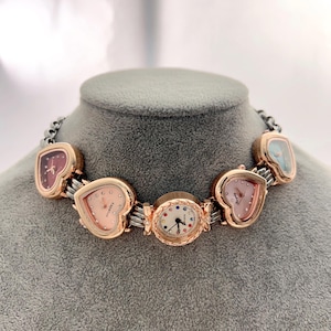 May include: A unique necklace featuring multiple watch faces in various shapes, including hearts and ovals. The watch faces have different colored dials and are set in gold-toned cases. The necklace is displayed on a gray mannequin head.