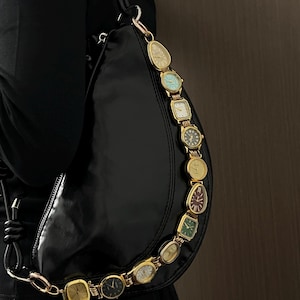 Könnte beinhalten: Schwarze, halbmondförmige Handtasche mit einem goldfarbenen Kettenriemen aus Vintage-Zifferblättern. Die Zifferblätter sind in verschiedenen Formen und Farben gehalten, darunter Gold, Grün und Blau. Die Tasche ist aus glänzendem, glattem Material.