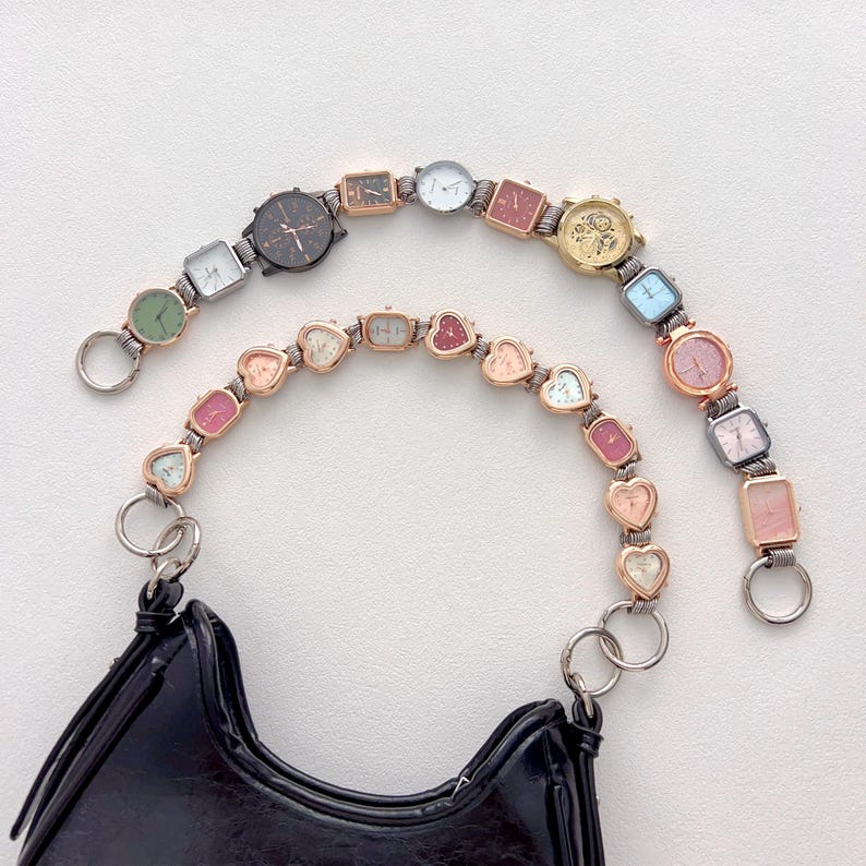May include: A black handbag with two decorative straps made of small, colorful watches. The watches have various shapes, including round, square, and heart-shaped, and feature different colored faces and metal finishes. The straps are attached to the bag with silver rings.