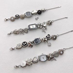 May include: Four silver charm bracelets with watch faces and decorative charms. Each bracelet features a different watch face shape and is adorned with various charms, including hearts, flowers, and pearls. The bracelets are displayed on a white surface.