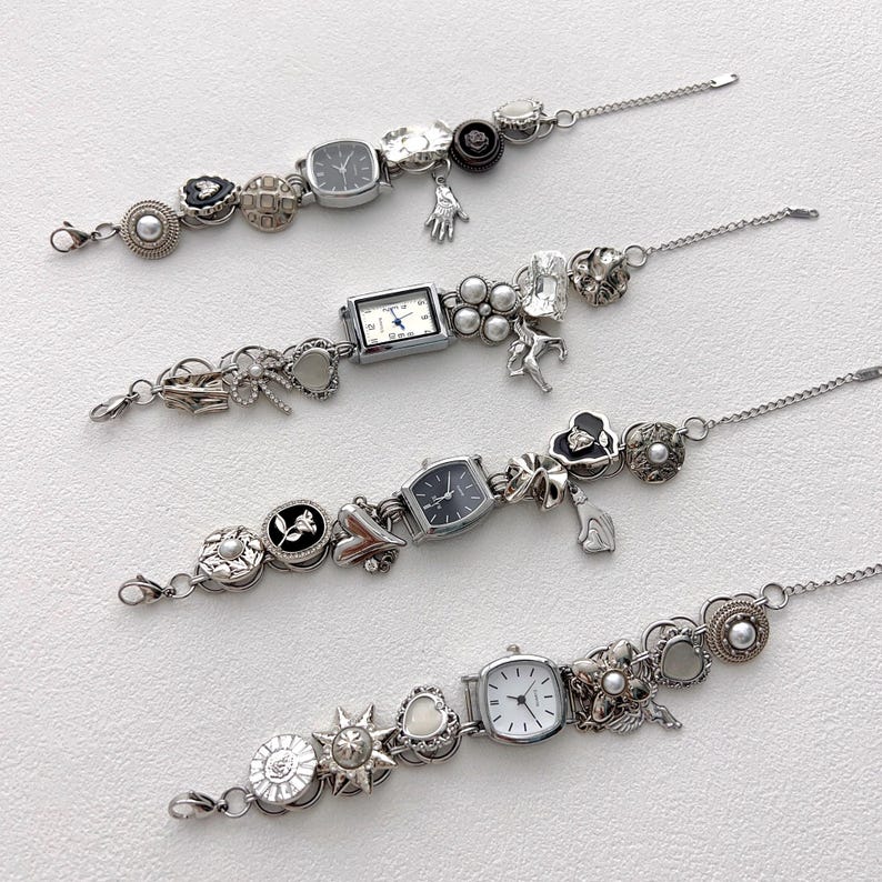 May include: Four silver charm bracelets with watch faces and decorative charms. Each bracelet features a different watch face shape and is adorned with various charms, including hearts, flowers, and pearls. The bracelets are displayed on a white surface.