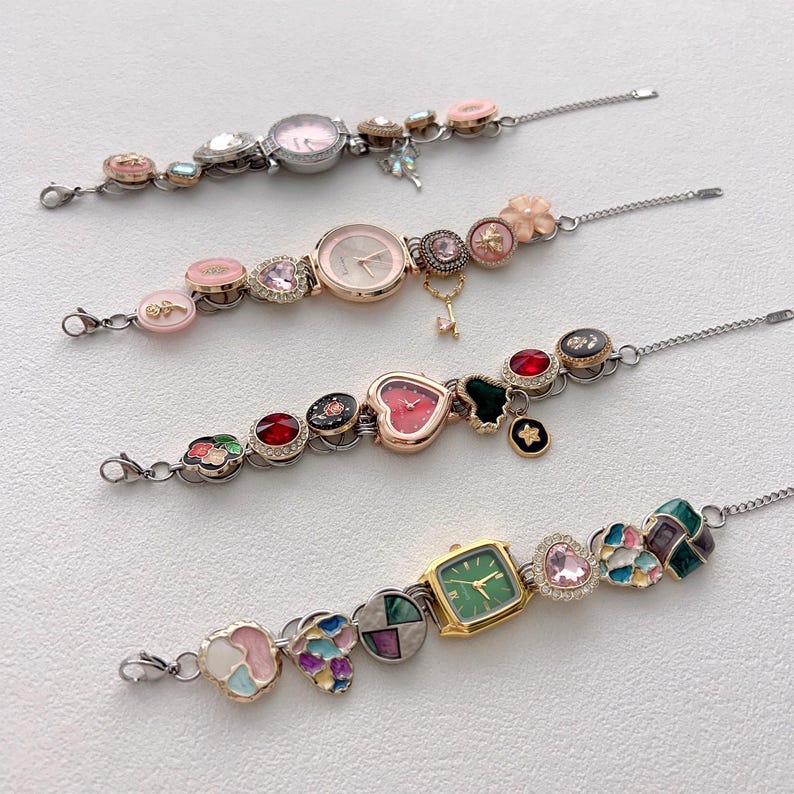 May include: Four decorative wristwatches with various embellishments. The watches feature round, heart, and square faces in pink, gold, and green. The bands are adorned with colorful charms, including hearts, flowers, and gemstones, and are connected by a silver chain.