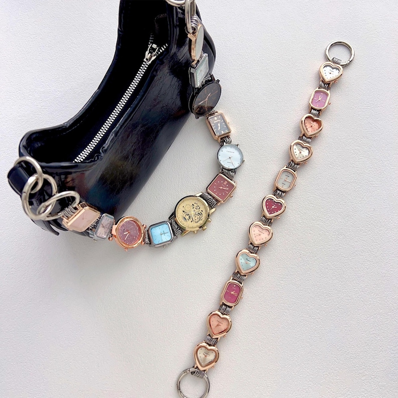 May include: A black handbag with a silver chain strap, adorned with a series of small, colorful watches. A separate watch strap with heart-shaped watch faces is also present. The watches feature various shapes and colors, creating a unique accessory.