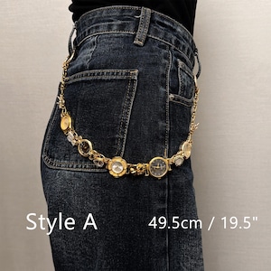 May include: A gold-toned watch chain belt, Style A, with multiple watch faces and decorative elements. The belt is 19.5 inches long and is worn on dark blue denim jeans. The text "Style A" and "49.5cm / 19.5" are visible.