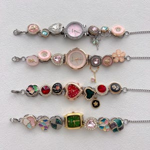 May include: Four decorative watch bracelets with various charms and watch faces. The bracelets feature pink, green, and red watch faces, along with heart, flower, and gem-shaped charms. The bracelets are connected by a silver chain.