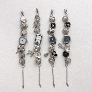 以下が含まれることがあります： さまざまな装飾要素を備えた4つのシルバーチャームブレスレット。各ブレスレットには、小さな時計、ボタン、パール、ハート、花、サンバーストなどのチャームが付いています。ブレスレットの下部にはチェーンが付いています。