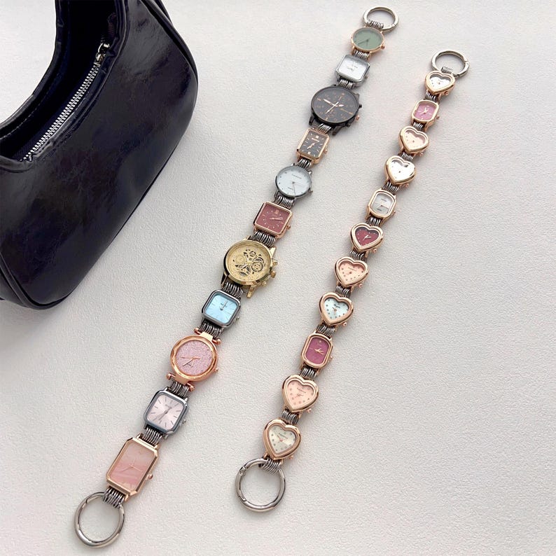 May include: Two watch straps with various watch faces, including square, rectangular, and heart-shaped designs. The straps are silver and gold-toned, with a black purse in the background. The watches have different colored faces.