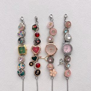 May include: Four decorative charm bracelets with various embellishments. Each bracelet features a watch face and decorative charms, including hearts, flowers, and gemstones. The bracelets are silver-toned with a variety of colors, including pink, green, and red.