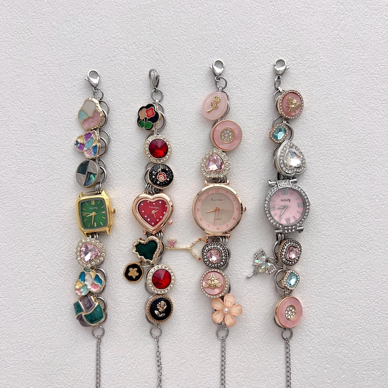May include: Four decorative charm bracelets with various embellishments. Each bracelet features a watch face and decorative charms, including hearts, flowers, and gemstones. The bracelets are silver-toned with a variety of colors, including pink, green, and red.