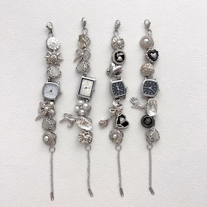 May include: Four silver charm bracelets with various decorative elements. Each bracelet features a small watch, buttons, pearls, and charms like hearts, flowers, and sunbursts. The bracelets have a chain at the bottom.