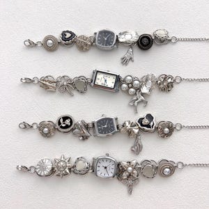 May include: Four silver charm bracelets with various charms, including small watches, hearts, flowers, and other decorative elements. The bracelets are displayed on a white surface, showcasing the intricate details of each piece.