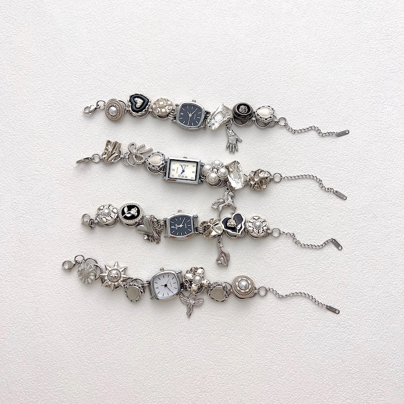 May include: Four silver-toned charm bracelets with watch faces and decorative charms. Each bracelet features a different watch face shape and a variety of charms, including hearts, flowers, and pearls. The bracelets are displayed on a white surface.