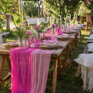 Puede incluir: Una larga mesa de madera preparada para un evento al aire libre, adornada con caminos de mesa rosas y magenta, platos y arreglos florales. Altas velas blancas y vasos transparentes completan el elegante escenario. La escena se desarrolla en un jardín.