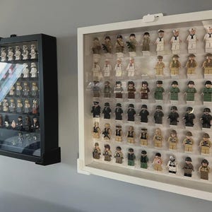 May include: Two wall-mounted display cases containing collections of small plastic toy figures. The left case is black with a glass front, while the right case is white with a glass front, both featuring multiple horizontal shelves for organizing figures.