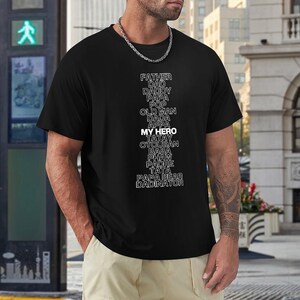 May include: Black t-shirt with the words "FATHER, DAD, DADDY, PAPA, POP, OLD MAN, DADA, APPA, MY HERO, TATAY, OTOUSAN, BABA, PHAW, PADRE, TATA, PAPA BEAR, DADINATOR" in white. The shirt is a crew neck.