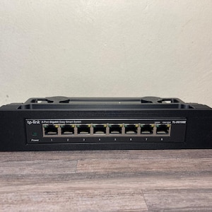 May include: Black 8-Port Gigabit Easy Smart Switch by tp-link. The device has eight Ethernet ports and a power indicator. The model number is TL-SG108E. The switch is designed for network connectivity.