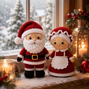 Puede incluir: Dos muñecos de ganchillo que representan a Santa Claus y a la Señora Claus. Santa viste un traje rojo con ribetes blancos, un cinturón negro con hebilla amarilla y un gorro rojo. La Señora Claus lleva un vestido rojo con un delantal blanco.