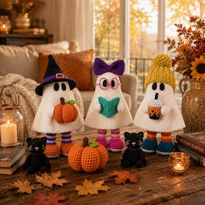 Puede incluir: Tres figuras de fantasmas de ganchillo con accesorios: una con sombrero de bruja negro sosteniendo una calabaza, otra con lazo morado y gafas rosas sosteniendo un libro, y otra con gorro de pompón amarillo sosteniendo un té boba, más dos gatos negros.