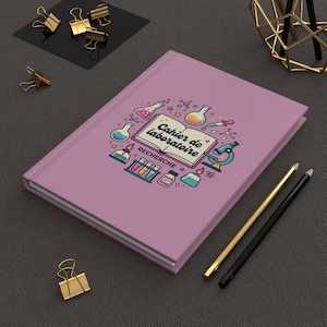 Peut inclure: Un carnet violet clair avec une illustration centrale représentant un livre ouvert portant le texte Cahier de laboratoire et RECHERCHE, entouré de dessins colorés d'équipements de laboratoire comme des béchers, fioles et un microscope.