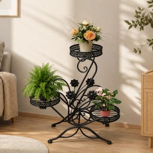 May include: A black metal plant stand with three circular shelves, each holding potted plants. The stand has a decorative floral design and a curved, ornate structure. The plants include ferns and flowering plants.