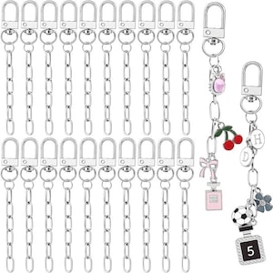 May include: A collection of silver-colored keychains with lobster claw clasps and chain links. Several keychains are plain, while others feature decorative charms, including a pink bow, a perfume bottle, cherries, and a soccer ball.