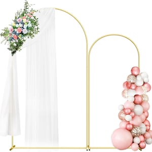 May include: A gold metal double arch backdrop stand featuring a tall arch draped with white sheer fabric and a floral arrangement, and a shorter arch decorated with a cluster of pink, white, and gold confetti balloons for event decoration.