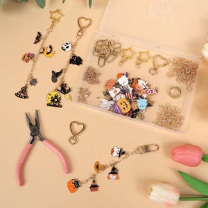 May include: A DIY jewelry making kit featuring gold-tone metal chains, lobster clasps, and heart-shaped clips. Includes various Halloween-themed enamel charms like pumpkins, ghosts, bats, and witch hats, alongside a pair of pink-handled pliers.