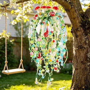 May include: A hanging garden ornament featuring a white base topped with four red and white mushroom figures. Numerous strands of multi-coloured glass beads in shades of green, blue, red, and yellow cascade downward, creating a vibrant, textured display.