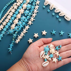 May include: A collection of loose beads and strands featuring white and turquoise blue starfish, sea turtles, and cowrie shells. The assortment includes small round beads and various marine-themed shapes, displayed both as individual pieces and on strings.