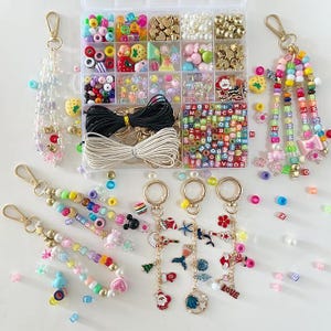 May include: A collection of colorful beaded keychains and a bead organizer. The keychains feature various charms, including hearts, stars, and cartoon characters. The organizer contains beads in various shapes, sizes, and colors, along with string and clasps.