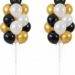 May include: Two balloon stands, each featuring a cluster of black, gold, and white balloons attached to a central white pole with a circular base. The balloons are arranged in a vertical display, creating a decorative column of metallic and matte colors.