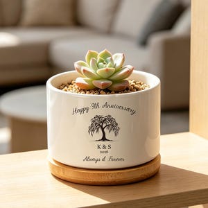 May include: A white ceramic planter with a succulent plant, sitting on a wooden coaster. The planter has the text "Happy 9th Anniversary" and a tree design. Below the tree is the text "K&S 2025 Always & Forever".