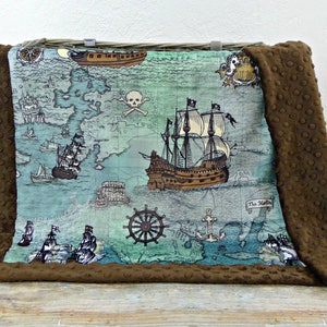 May include: A brown and blue pirate-themed blanket with a map design featuring ships, a skull and crossbones, and a ship's wheel. The blanket has a brown, textured border.