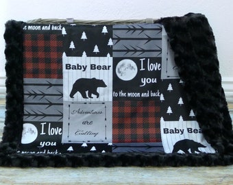 May include: A black and gray baby blanket with a patchwork design. The blanket features a black bear, a moon, and the text "Baby Bear", "I love you to the moon and back", and "Adventures are calling".