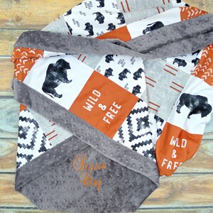 May include: A gray and white baby blanket with a patchwork design featuring buffalo silhouettes, geometric patterns, and the text "Wild & Free". The blanket has a soft, gray minky backing and is personalized with the name "Stetson Gray".