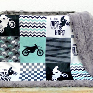 May include: A patchwork baby blanket with a motocross theme. The blanket features a variety of patterns, including checkered, chevron, and stripes. The blanket is made of soft, plush fabric and is perfect for cuddling up with. The blanket also features the text "A little dirt never hurt".