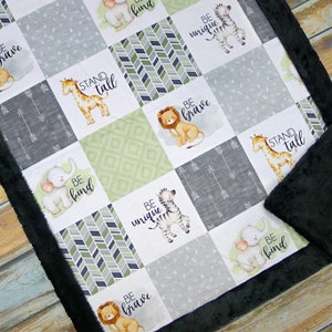 May include: A patchwork baby blanket with animal illustrations and motivational phrases. The blanket features a lion, giraffe, elephant, and zebra, with text that reads "Be Brave", "Stand Tall", "Be Kind", and "Be Unique". The border is black.