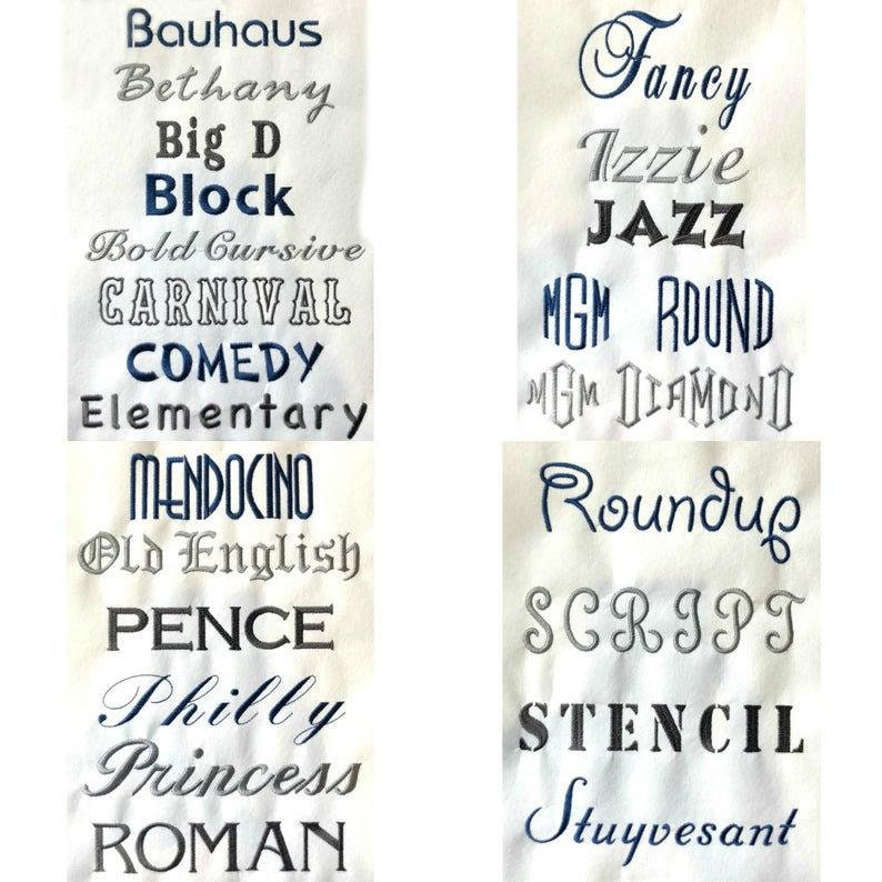 Pode incluir: Uma amostra de tecido branco com v&aacute;rios estilos de fonte de bordado, incluindo Bauhaus, Bethany, Big D, Block, Bold Cursive, Carnival, Comedy, Elementary, Mendocino, Old English, Pence, Philly, Princess, Roman, Fancy, Izzie, Jazz, MGM Round, MGM Diamond, Roundup, Script, Stencil e Stuyvesant.